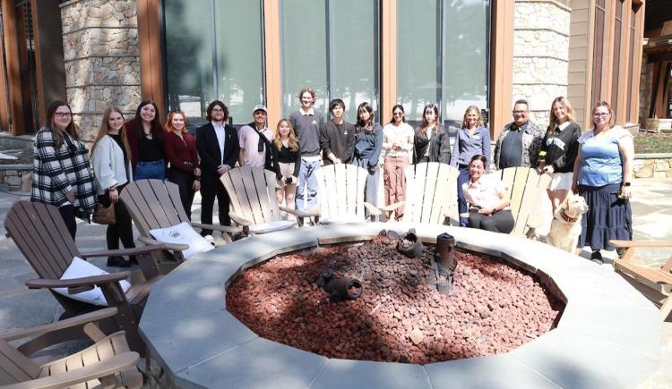 Hospitality and Tourism Management students with their instructor on a sunny day outside with a fire pit and wooden chairs in front at the Ritz-Carlton in Truckee, CA.
