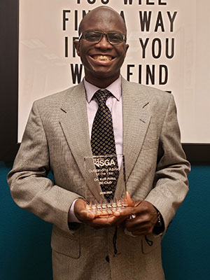 Dr. Poku, smiling, holds his award from the SGA.