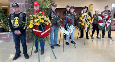 Vietnam War veterans stand beside colorful flower wreaths inside the Student Center.