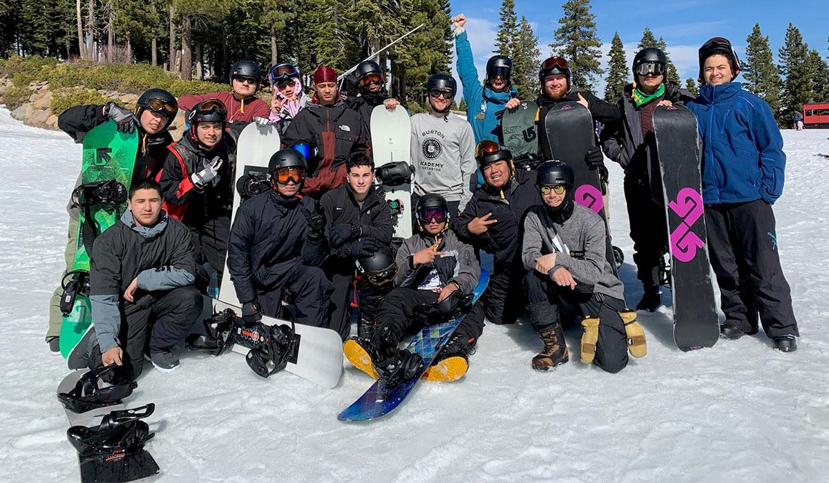 Group of students with skis and snowboards on a snowy mountain.