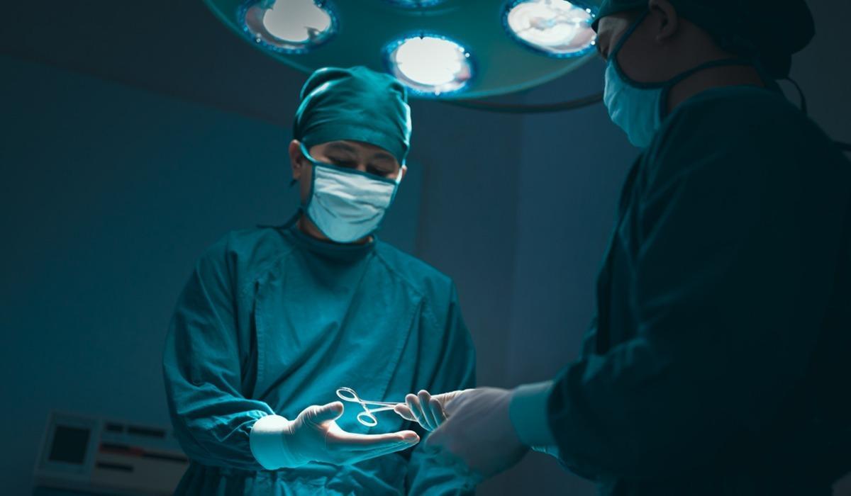 A surgical technologist hands medical scissors to the head surgeon during surgery.