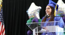 Photo of a student wearing graduation robes on a stage.