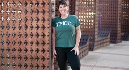 Monika Koshinski poses for a graduation photo outside, smiling and wearing a green TMCC t-shirt and black pants.