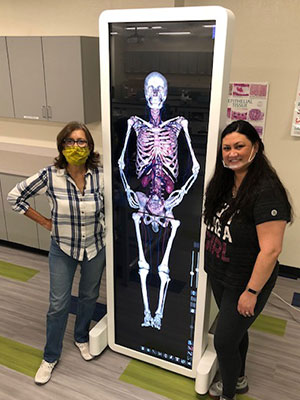 Vigil and student standing next to a large touchscreen with a human anatomical diagram displayed on it.
