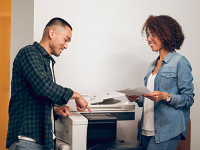 Two people using copier machine.