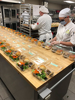 Students assembling a row of meals in takeout containers.