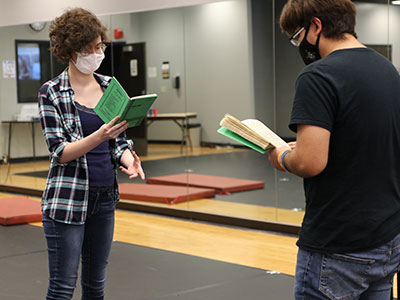 Two masked students reading script books.