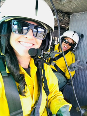 Julli Giampapa and another firefighter smile for the camera from inside a helicopter.