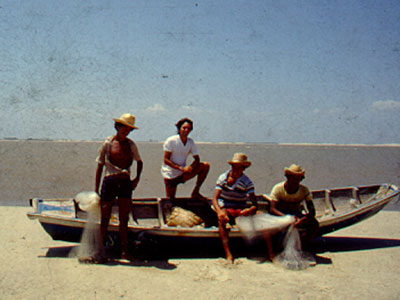 Four men standing in a fishing boat on a beach.