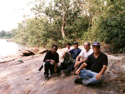 A group of men pose for a photo on the bank of a river.