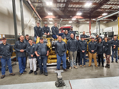 A group of 20 students smile for a photo in the diesel lab.