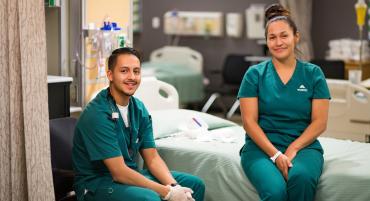 Student nurses relax by bedside in hospital setting.