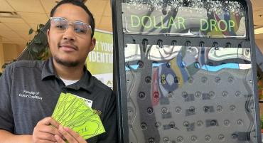 Student employee holds up fake cash at Financial Aid booth during OMG! Outrageous Money Games event.