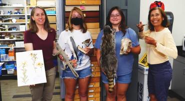 Drs. Megan Lahti and Cecilia Vigil stand beside students holding exhibits from the TMCC Natural History Museum.