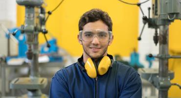 Engineering student smiles at the camera while wearing eye and ear protection in a workshop.