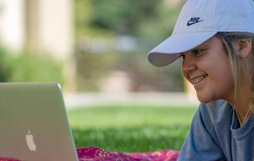 Student looks at her laptop computer outdoors.
