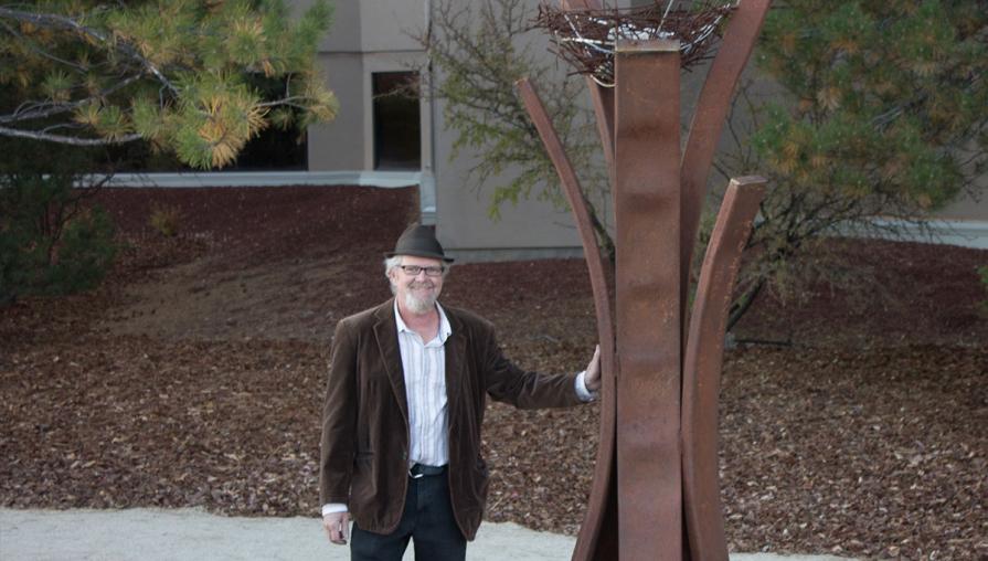 Artist and large metal sculpture outdoors.