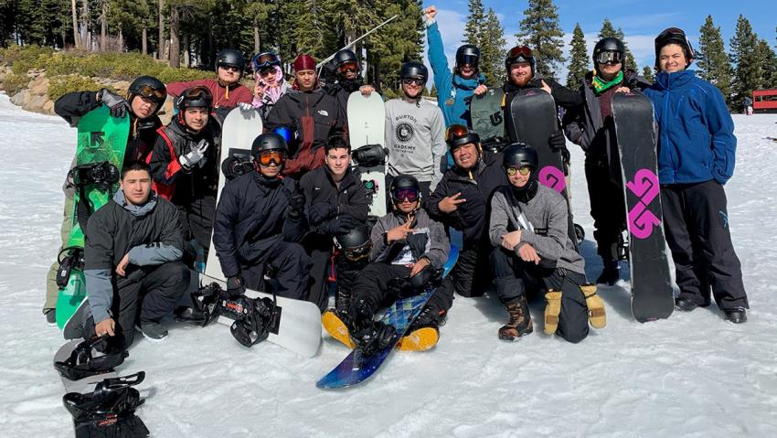 Group of students with skis and snowboards on a snowy mountain.