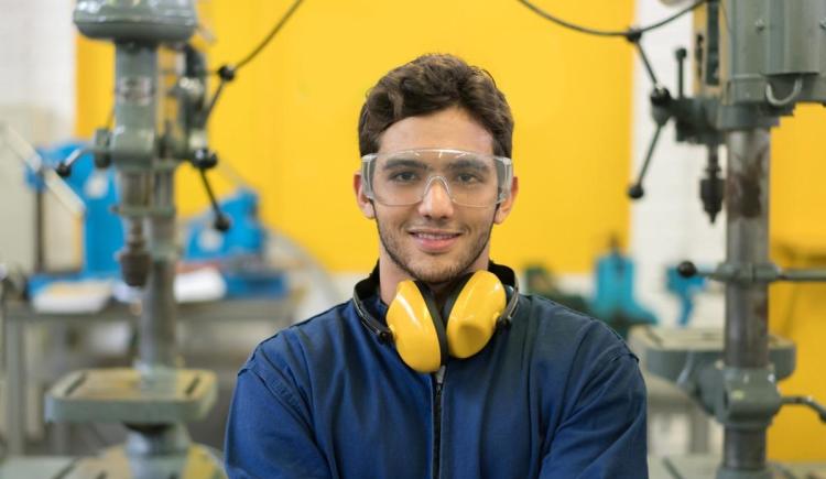 Engineering student smiles at the camera while wearing eye and ear protection in a workshop.