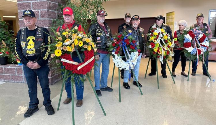Vietnam War veterans stand beside colorful flower wreaths inside the Student Center.