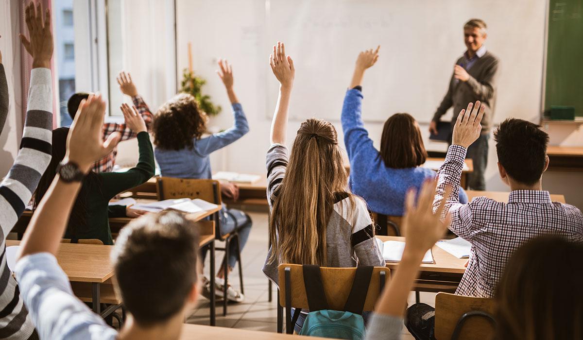 Students raising their hands in a classroom.