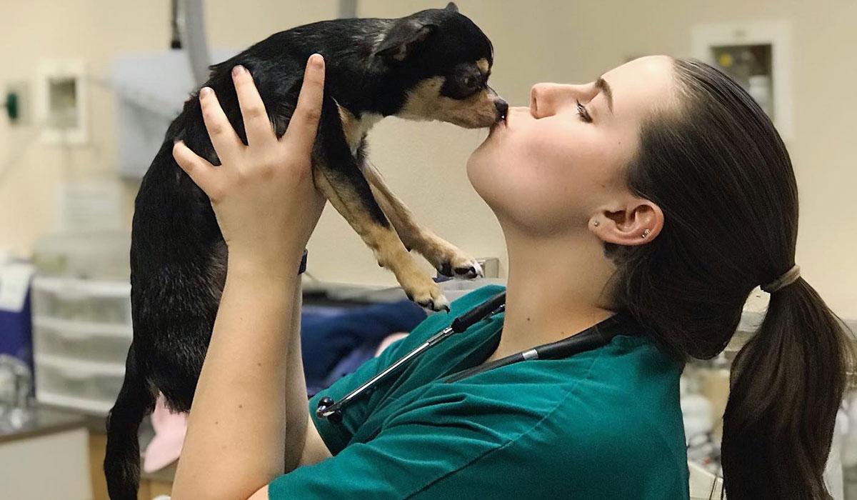 Veterinary nurse kisses a small puppy.