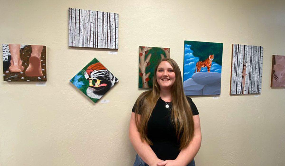TMCC Student Krista Gayer in front of a display of her artwork.
