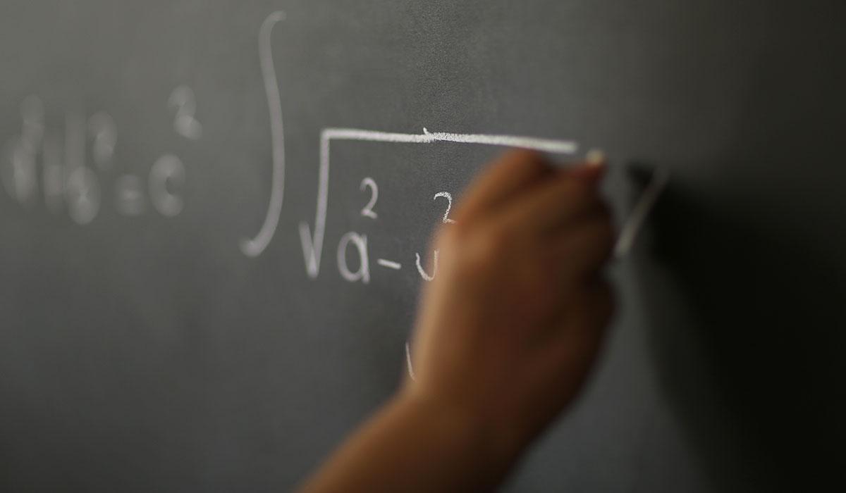 Photo of a hand writing an equation on a chalkboard.