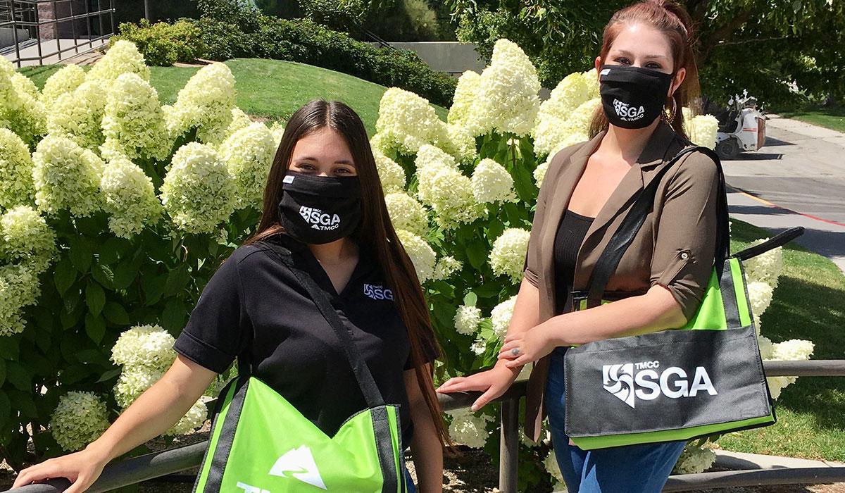 Two students wear masks while posing with SGA bags.