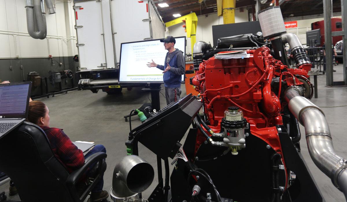 Kyle Smith lecturing next to an engine in the TMCC Diesel lab.