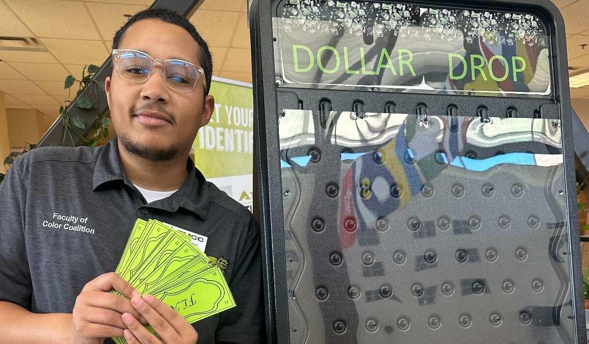 Student employee holds up fake cash at Financial Aid booth during OMG! Outrageous Money Games event.