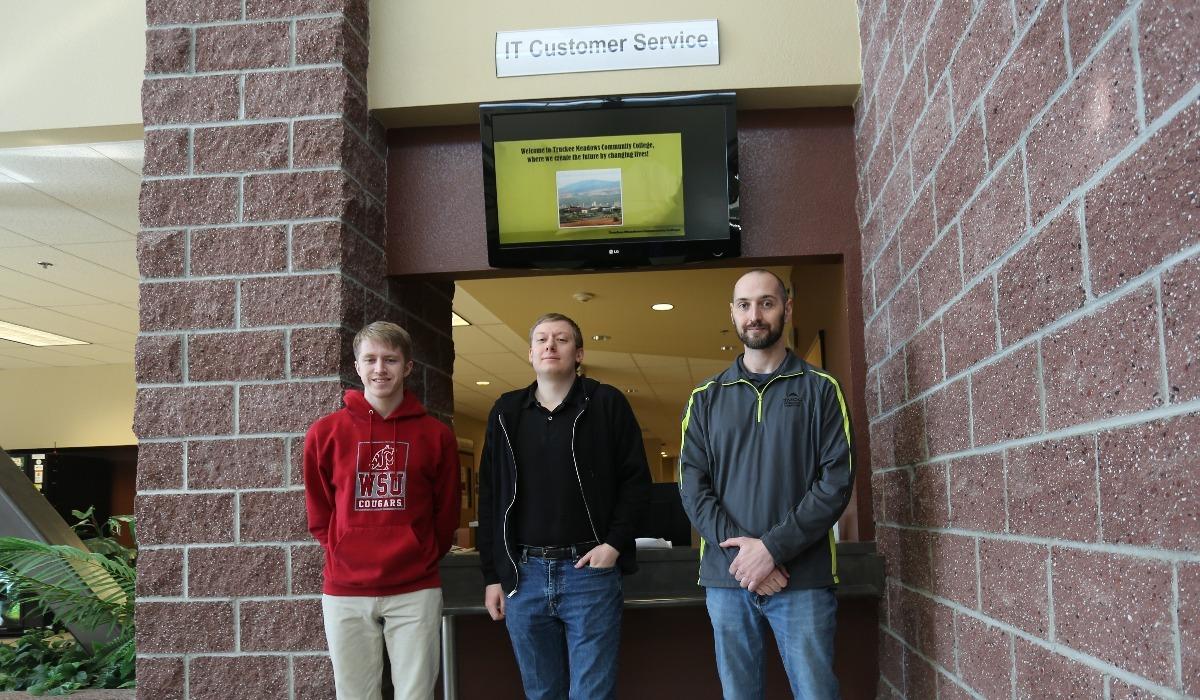 Ryan, Duncan, and Paul of Information Technology stand beside an IT Customer Service plaque.