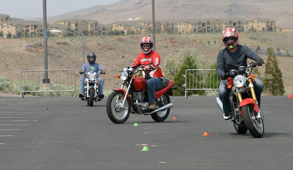 Students riding motorcycles in parking lot training session.
