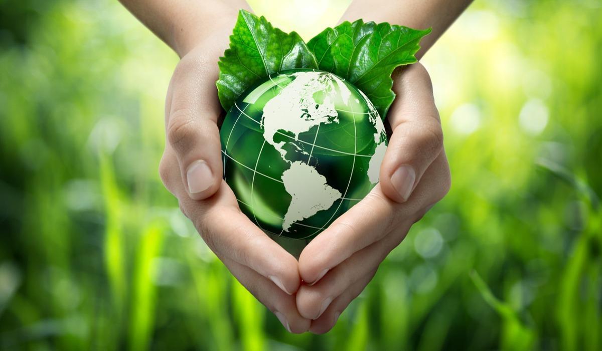 Hands in the shape of a heart hold a green globe with leaves resting on it.