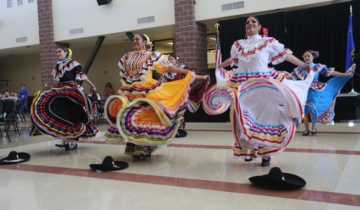 Six Hispanic women in traditional attire are dancing in the Student Center for the Tu Bienvenida event.