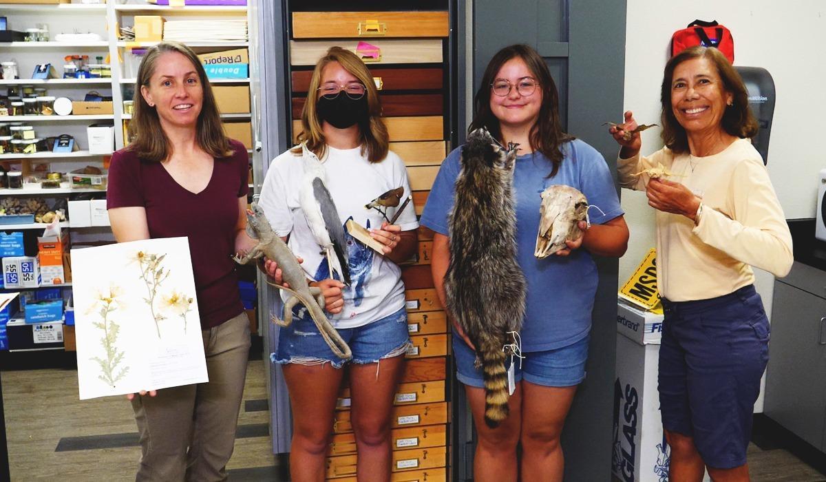 Drs. Megan Lahti and Cecilia Vigil stand beside students holding exhibits from the TMCC Natural History Museum.