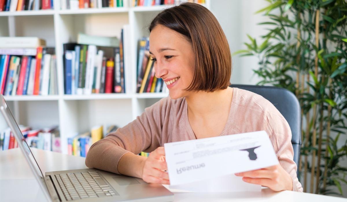 A college student smiles at her laptop with a completed resume in hand.
