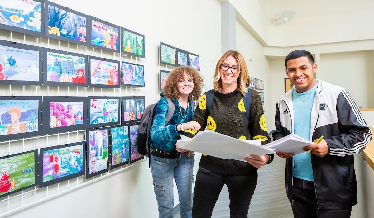 Students smile for a photograph next to artwork in the Sierra Building.