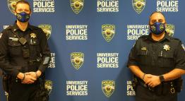 Two police officers standing in front of a University Police Services banner.