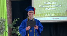 Caden Kuster holding up a degree dressed in graduation garb. 