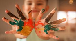 child with paint on his hands poses for the camera