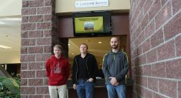 Ryan, Duncan, and Paul of Information Technology stand beside an IT Customer Service plaque.