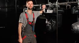 A theatre technician stands next to a lighting rig on a stage set.