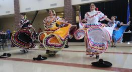 Six Hispanic women in traditional attire are dancing in the Student Center for the Tu Bienvenida event.