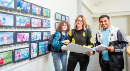 Students smile for a photograph next to artwork in the Sierra Building.