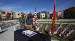 Kealii Kalawao-Cummings stands beside a colleague outside as the American and Marine Corps flags stand tall, and a cake lies flat on the table.